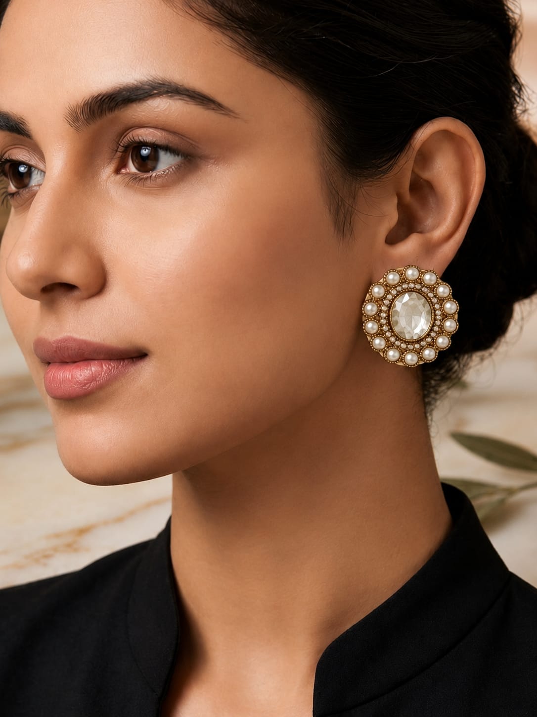 A close-up of a woman wearing a large, round gold-toned statement earring adorned with white pearls and a central white stone.