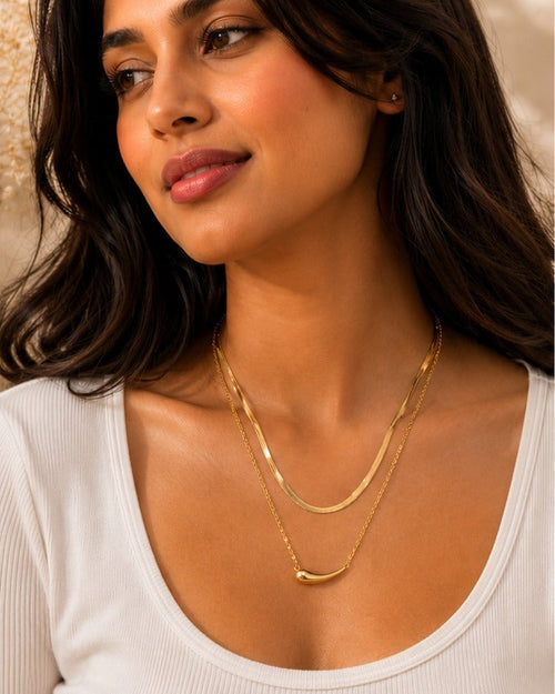 Woman wearing a gold necklace with a close-up of the necklace on a textured surface.